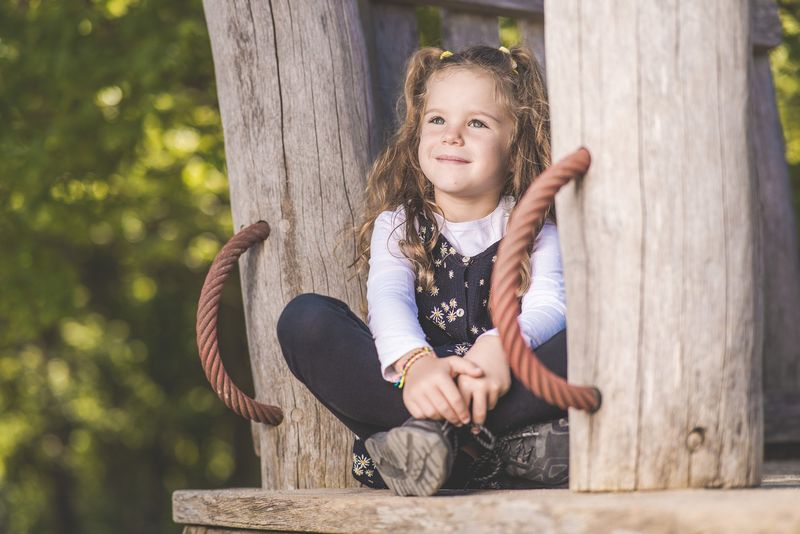 Kindergartenfoto: Mädchen sitzt lachend auf einer Holzbank im Außengelände der Kita
