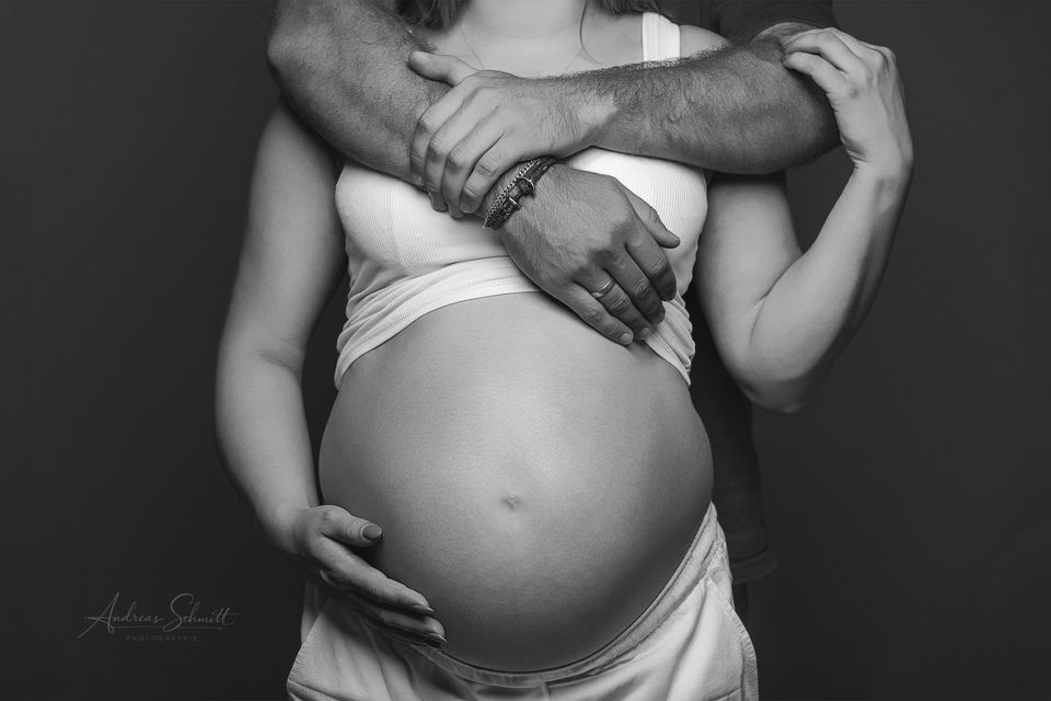 Babybauch-Foto in Schwarzweiß, der Partner umarmt die Schwangere