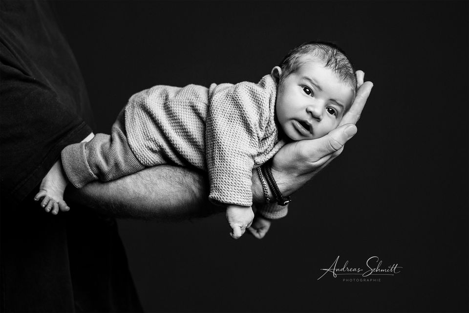 Baby liegt auf dem Arm des Vaters und schaut in die Kamera