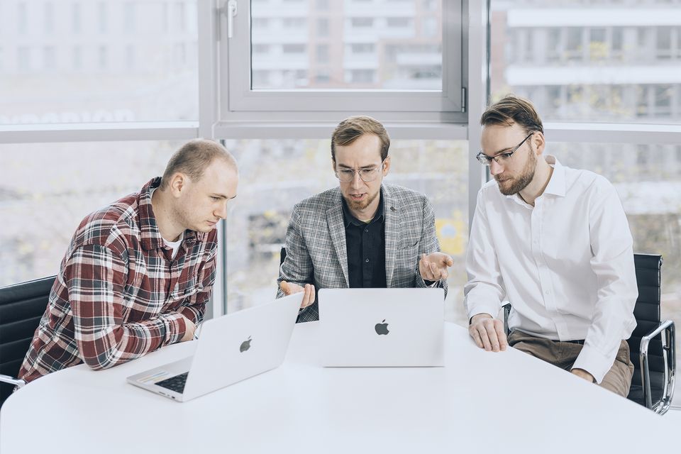 Drei Männer an einem Besprechungstisch mit Laptops