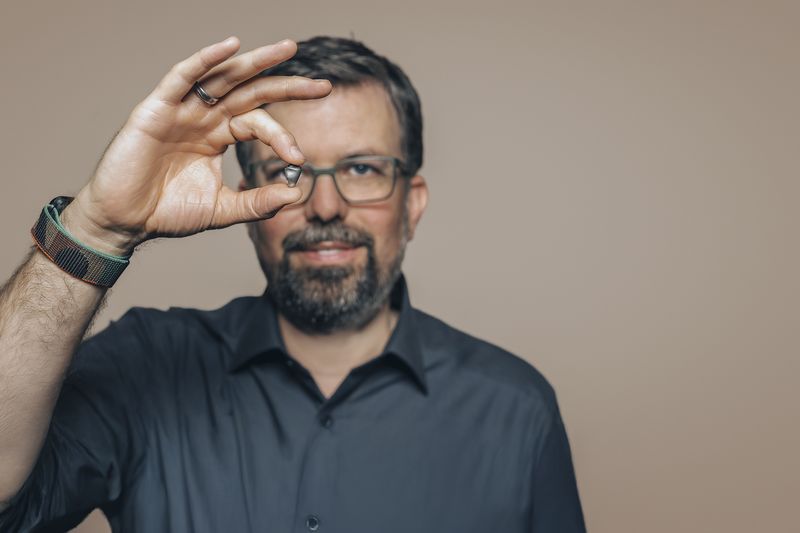 Mann mit Brille hält ein Objektiv vor das Auge