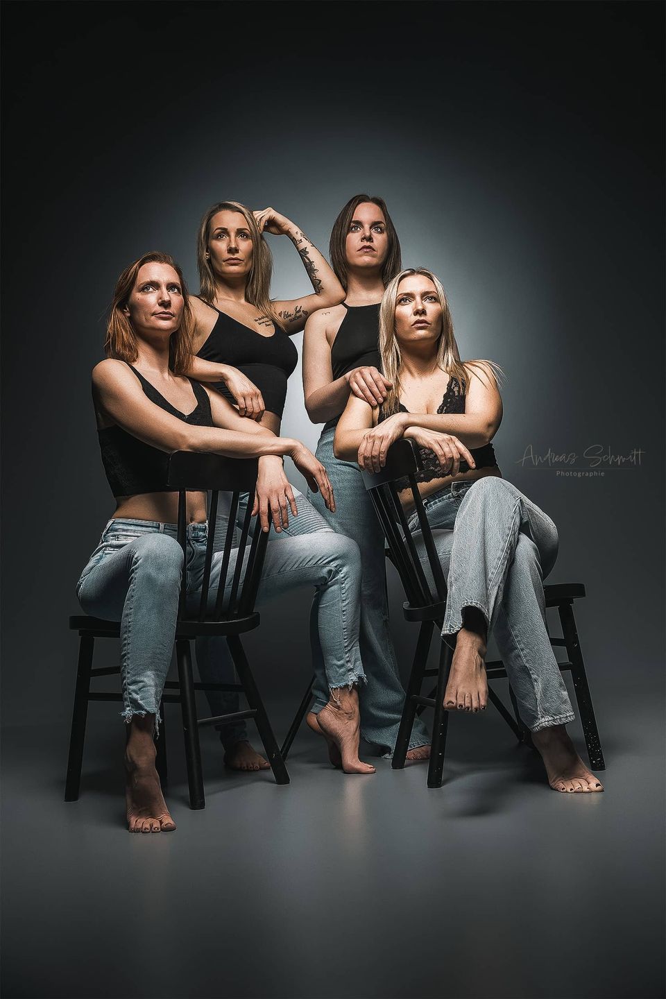 vier Frauen in Jeans und schwarzen Tops auf einem Gruppenfoto vor grauen Hintergrund.jpg
